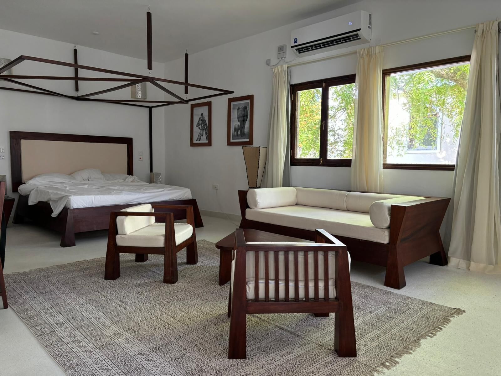A modern hotel room with a bed, a sofa, a chair, and a large window with curtains.