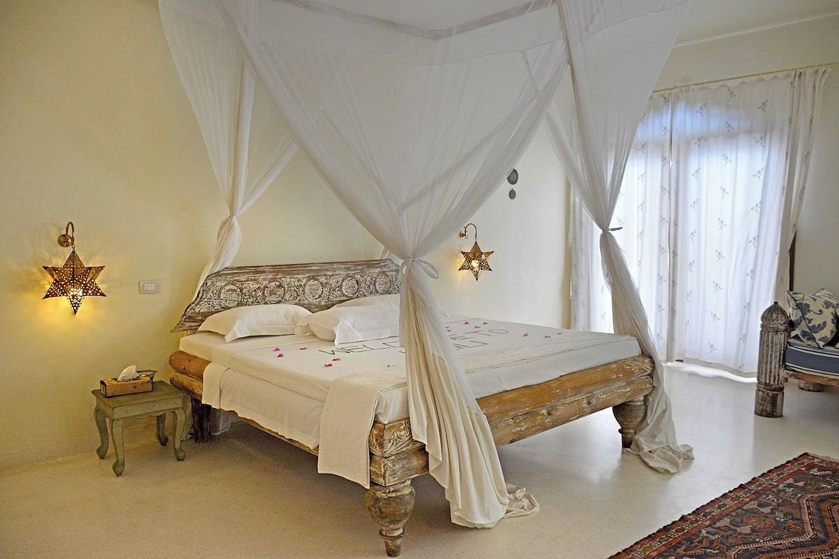 A bedroom with a four-poster bed, a nightstand, and a decorative star hanging from the bed.
