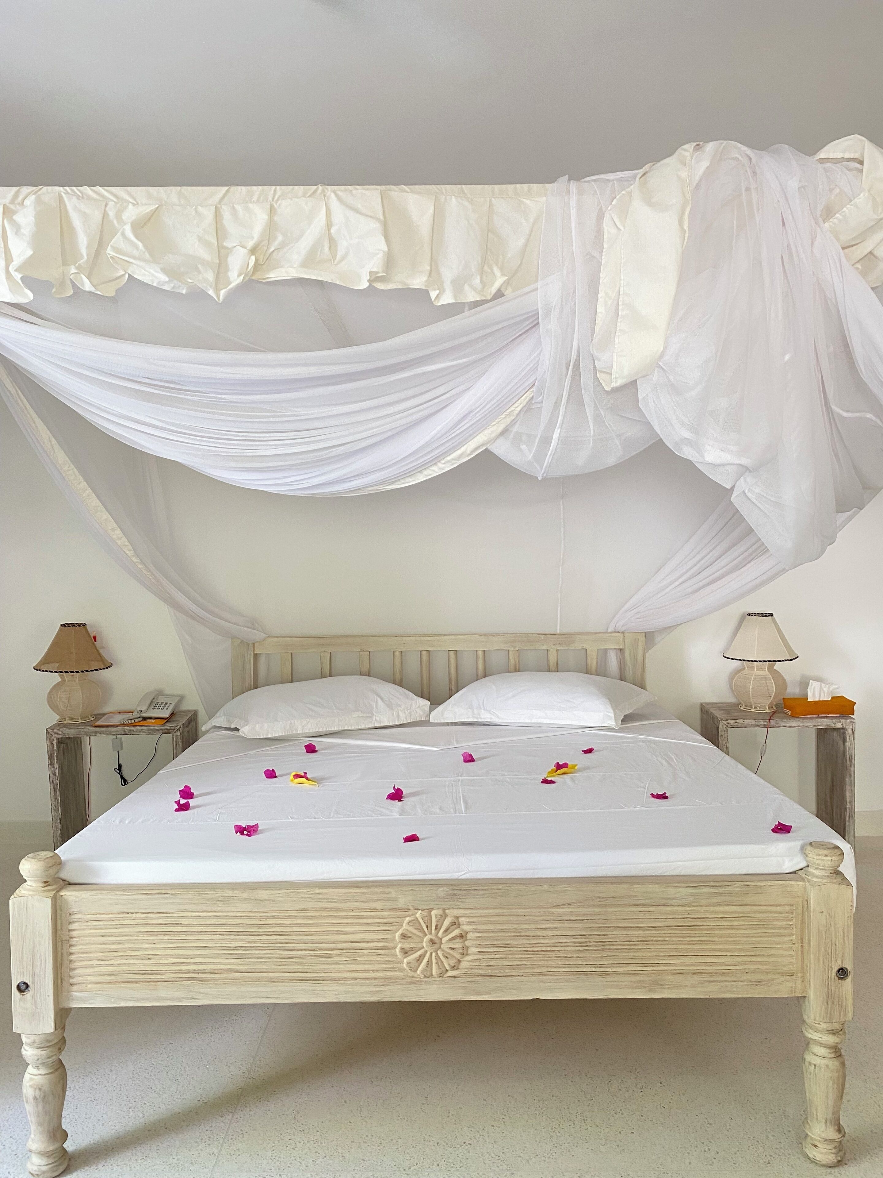 A bed with a canopy, white bedding, and scattered rose petals.