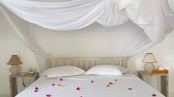 A bed with a canopy, white bedding, and scattered rose petals.