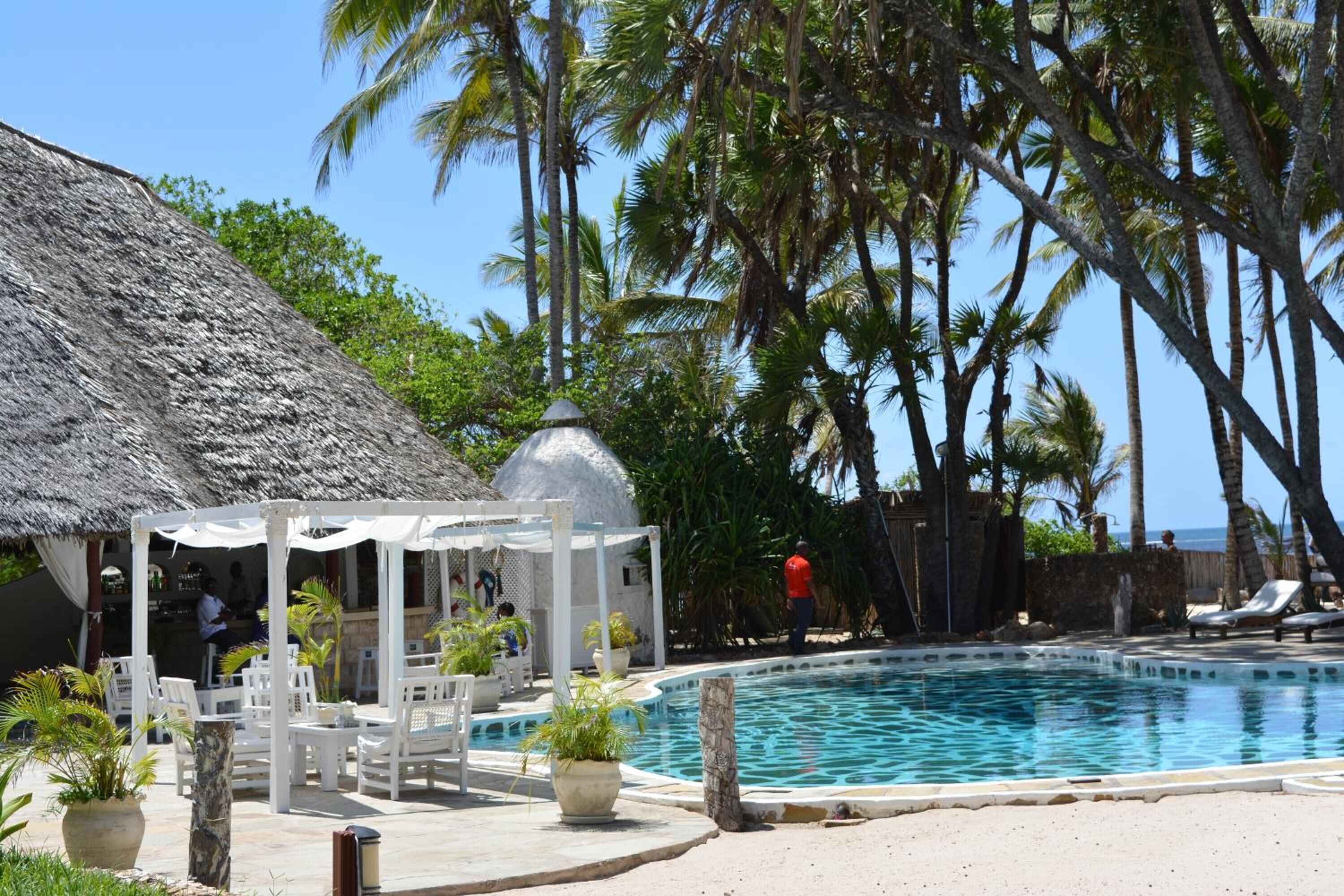 A poolside area with a thatched-roof structure, white lounge chairs, and a pool.