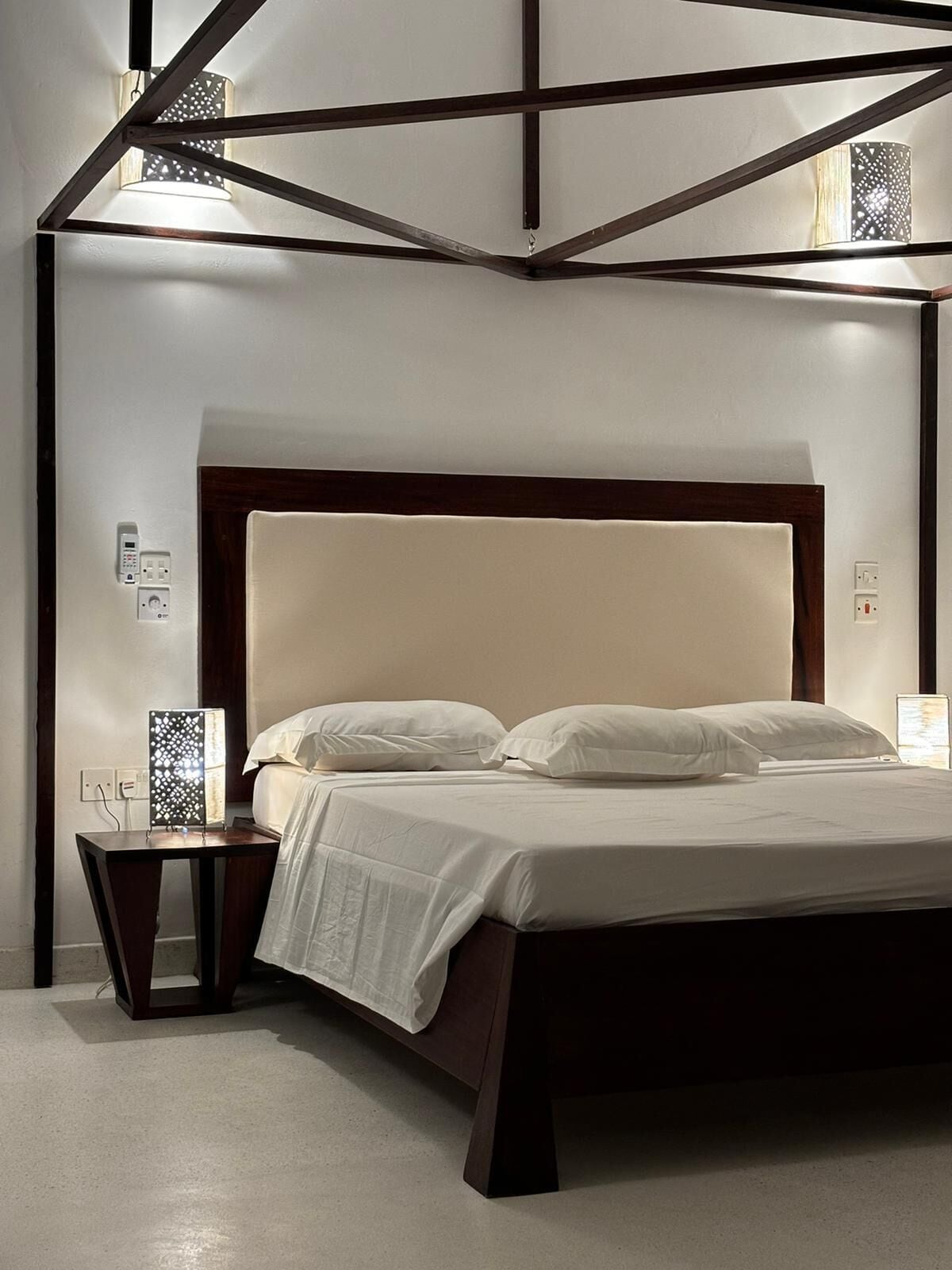 Un dormitorio moderno con una cama grande, una mesita de noche y una lámpara fijada en la pared.