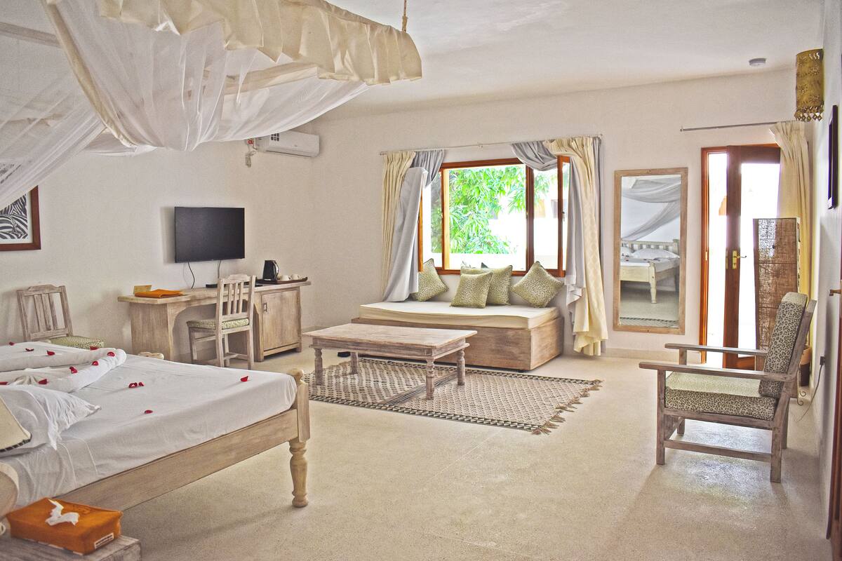A bedroom with a bed, a desk, a chair, a television, and a window with curtains.