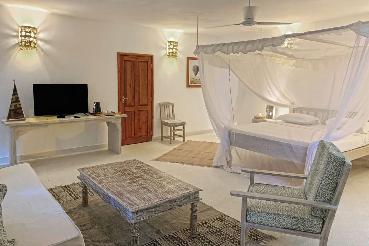 A bedroom with a bed, a TV, a wooden desk, a chair, and a ceiling fan.