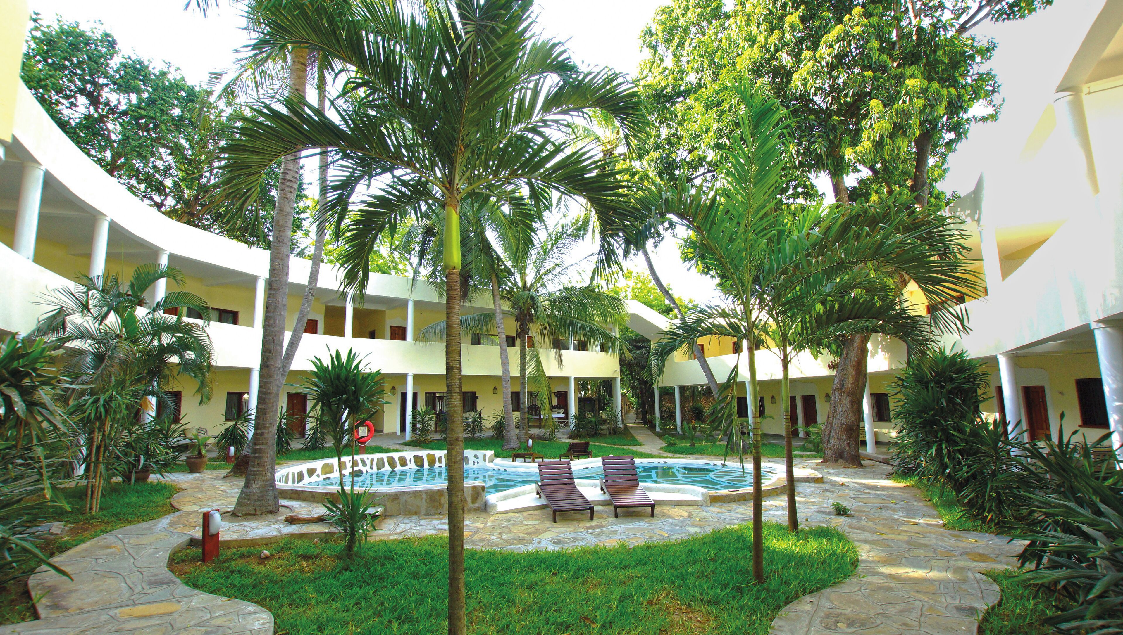 A hotel courtyard with a swimming pool, palm trees, and lounge chairs.