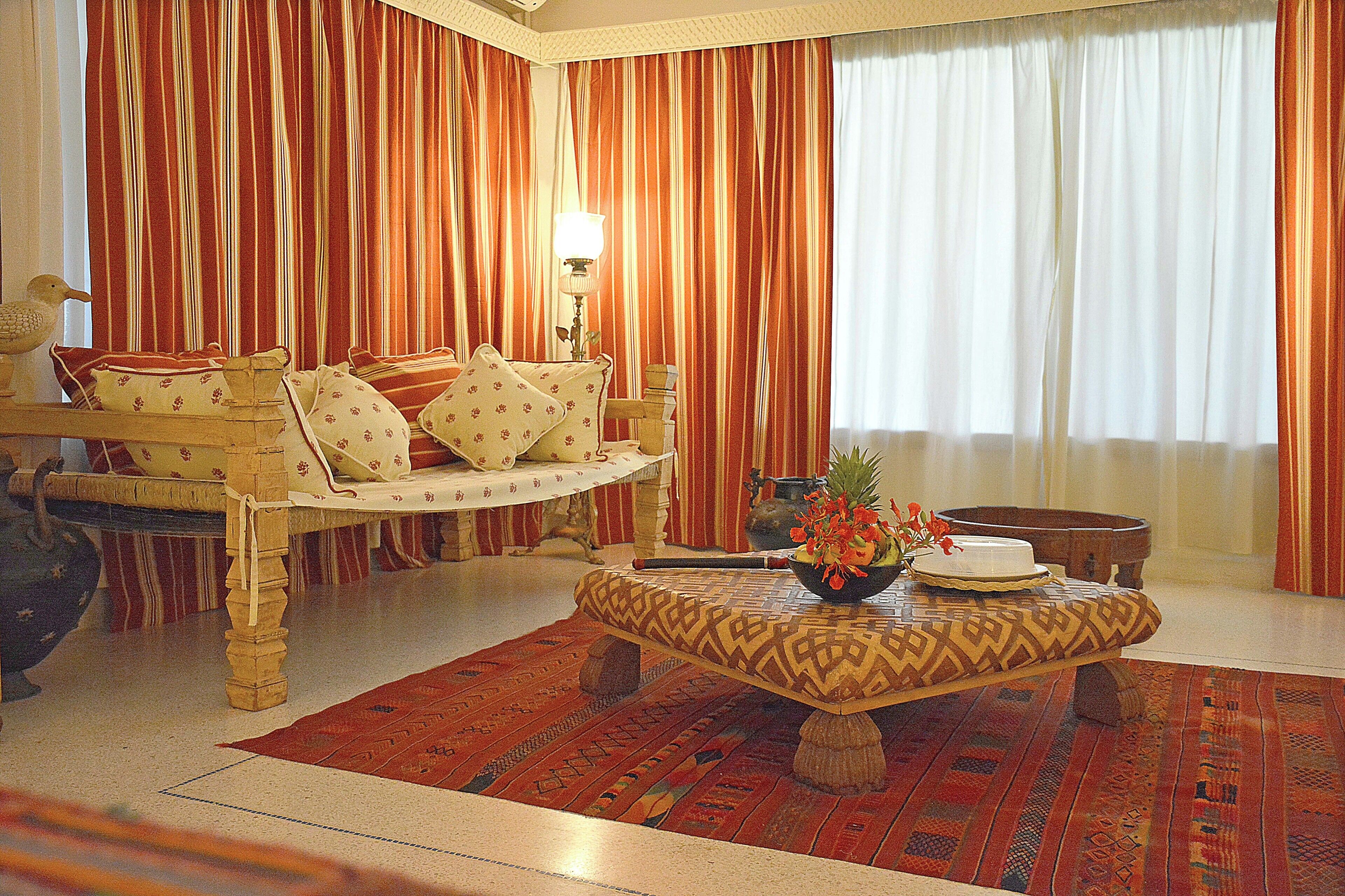 A room with a sofa set, a patterned ottoman, and a table with a flower vase.