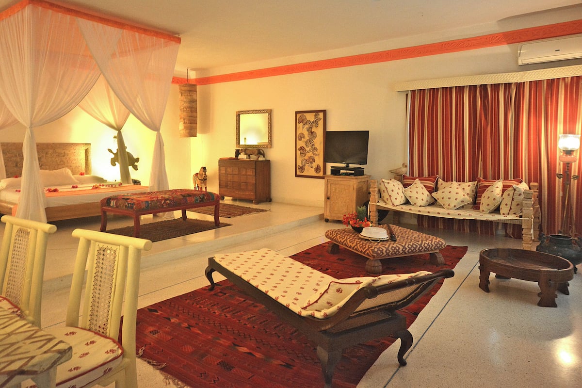 A hotel room with a bed, a sofa, a TV, and a dining area with chairs and a table.