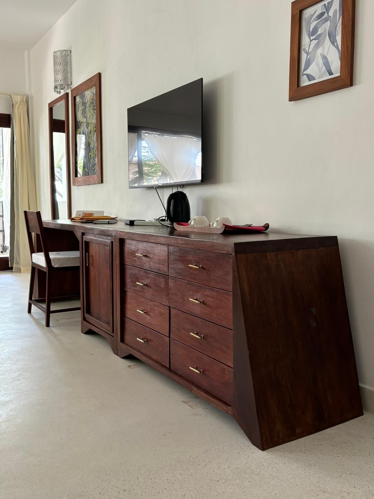 A modern room with a wooden desk, a flat-screen TV mounted on the wall, and a large window with curtains.