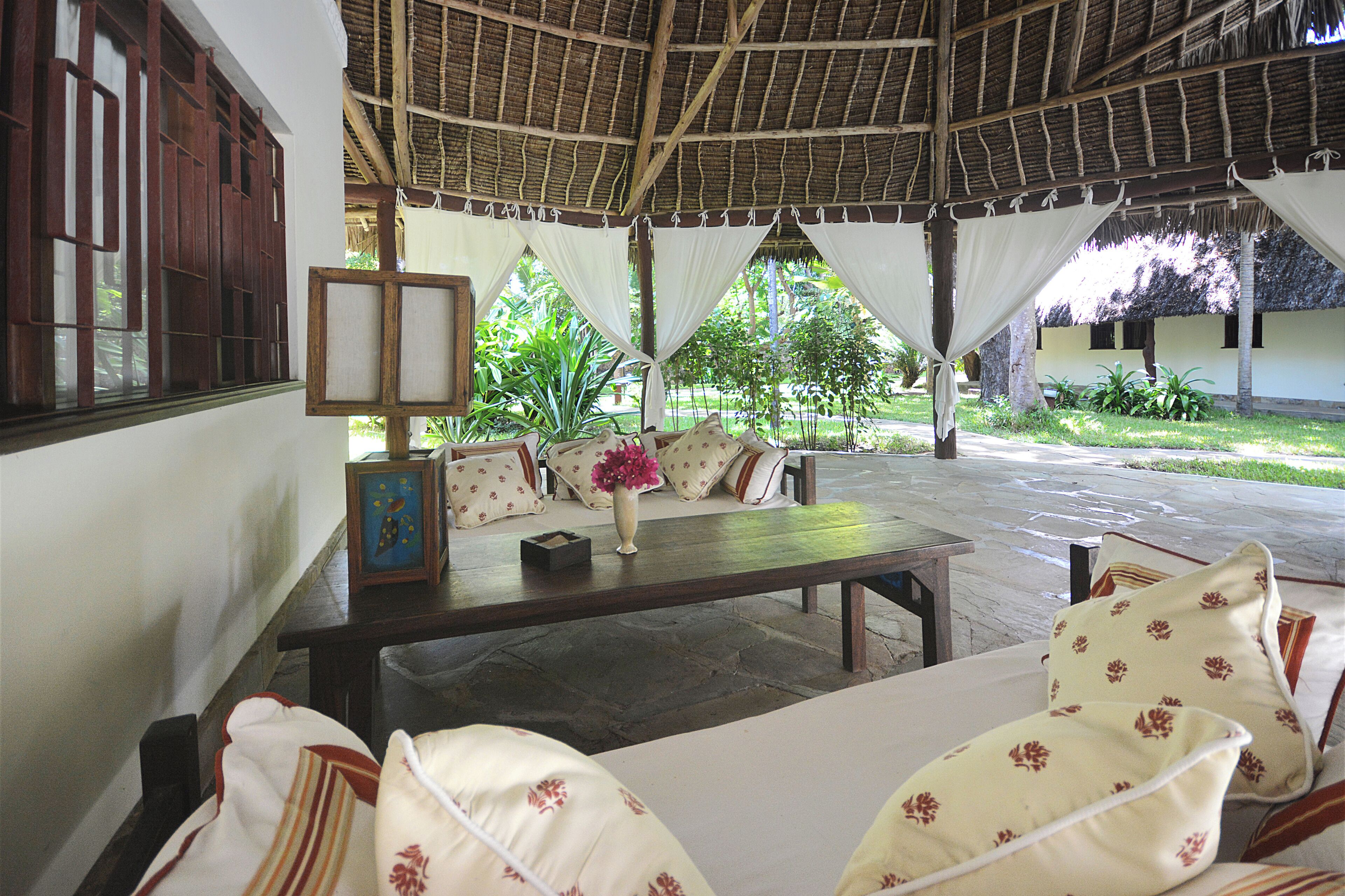 A covered outdoor seating area with a table, chairs, and a vase of flowers.