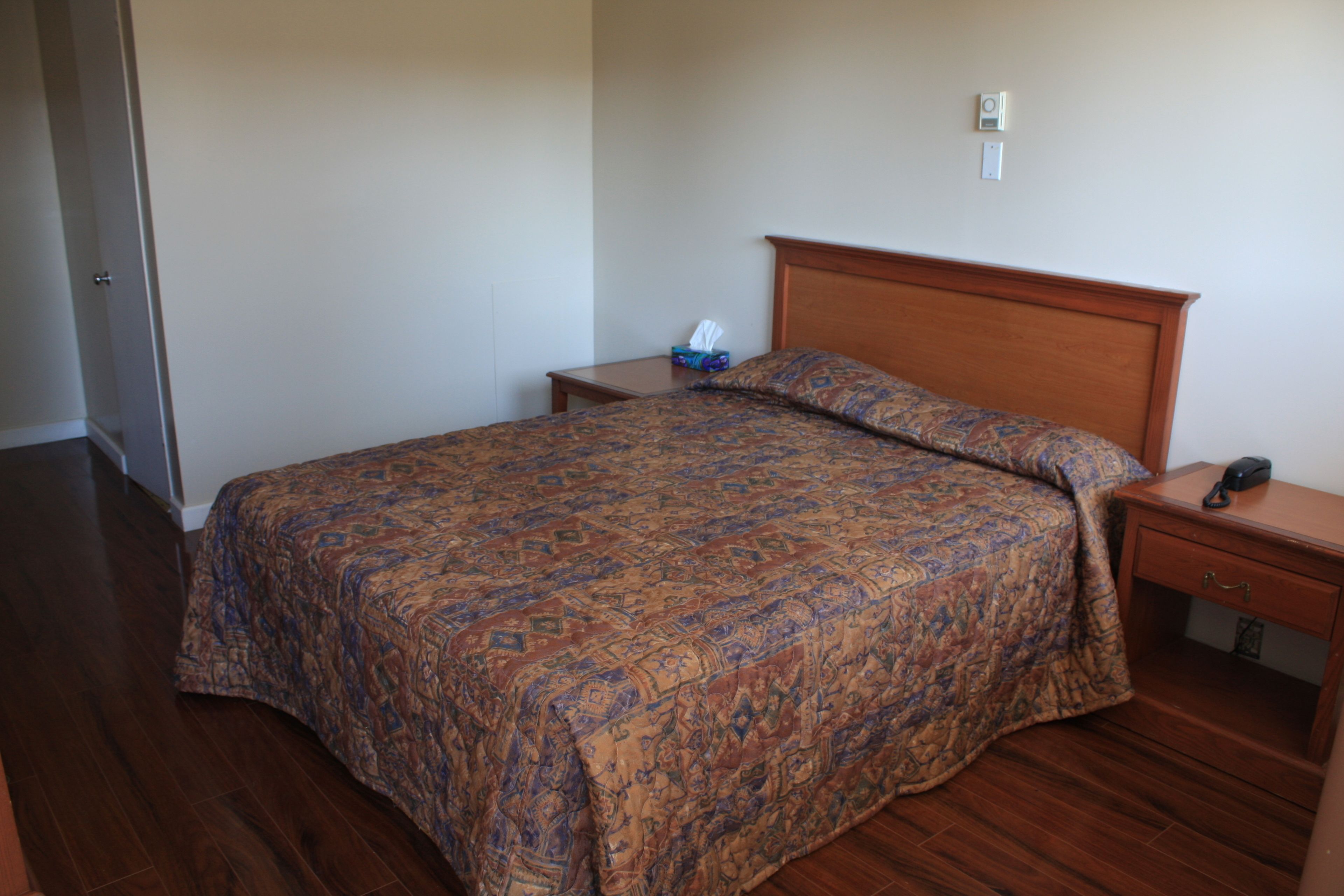Un dormitorio con una cama grande, cabecera de madera, una mesita de noche con una lámpara y una mesita auxiliar con una caja de pañuelos.