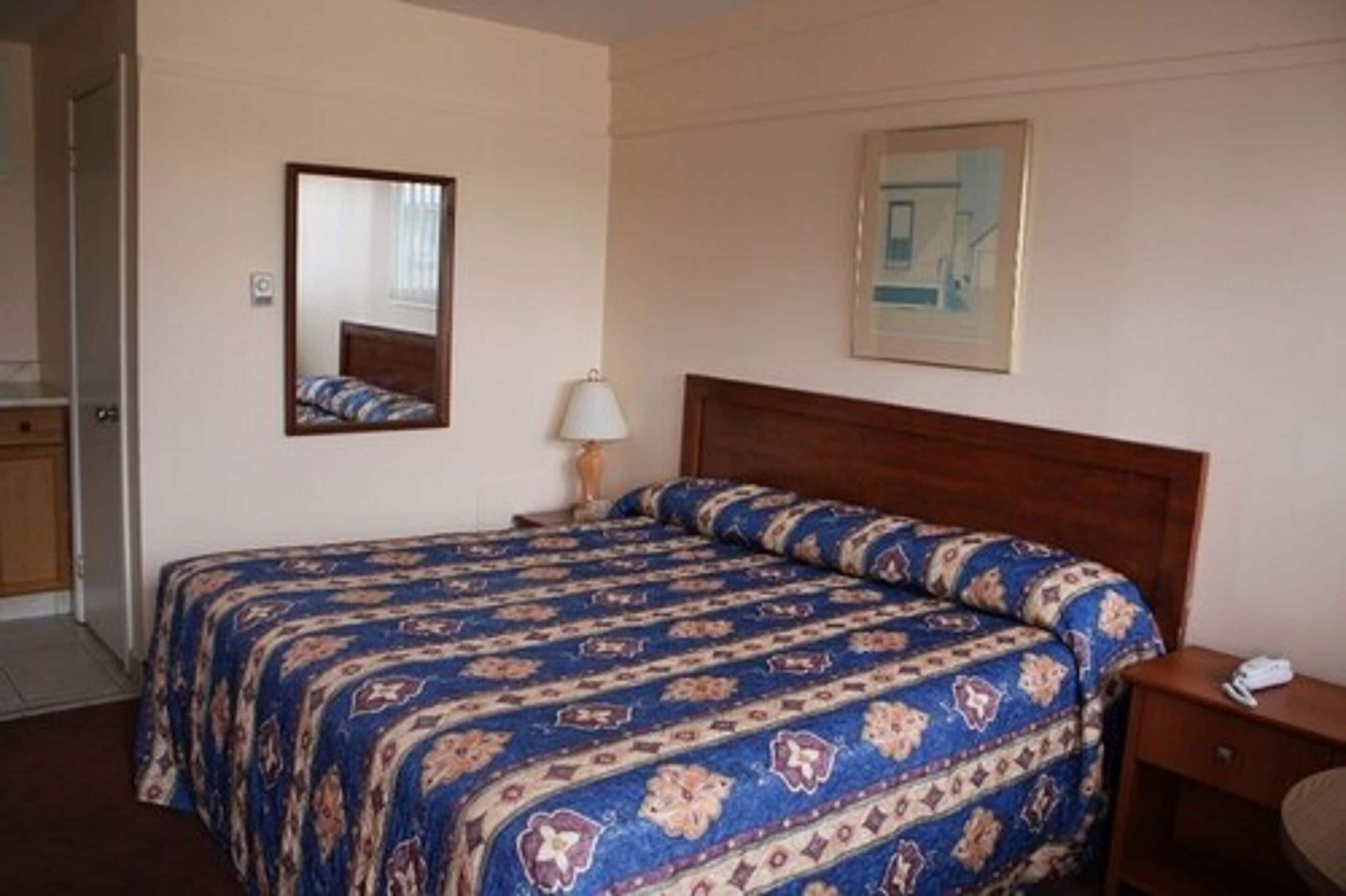 Ett hotellrum med en säng, ett sängbord, en lampa, en spegel och en inramad tavla på väggen.