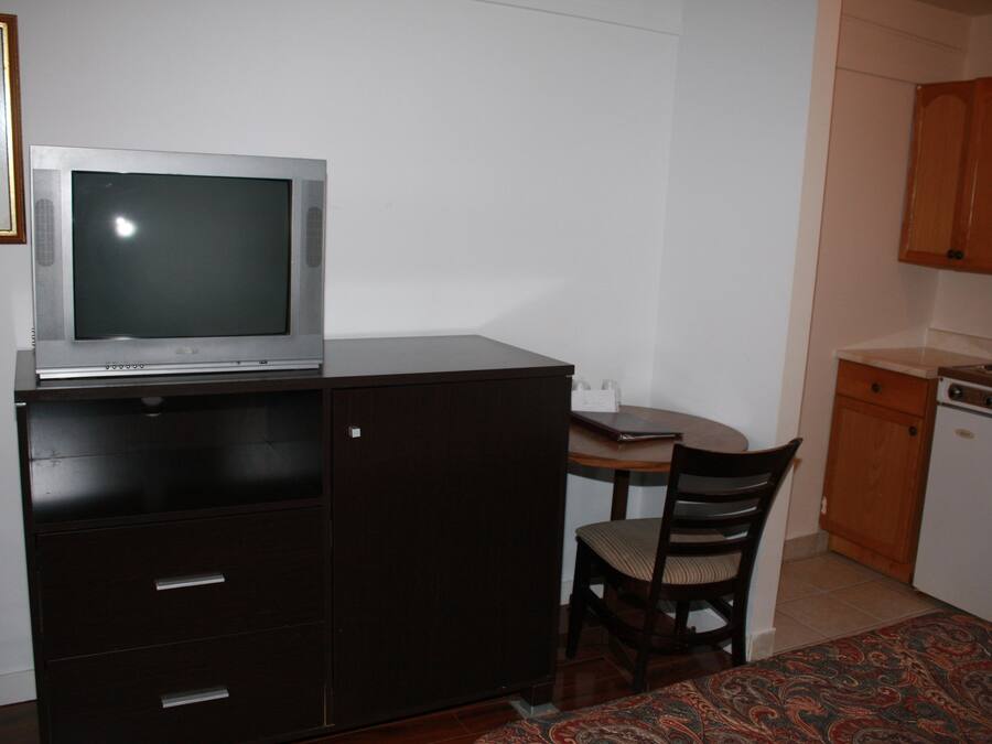 A compact kitchen with a microwave, a small refrigerator, a dining table with chairs, and wooden cabinets.
