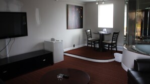 A modern living room with a flat-screen TV, a glass-enclosed hot tub, a dining area with chairs, and a small table. - Grand Motel Saint-Hubert (Longueuil)