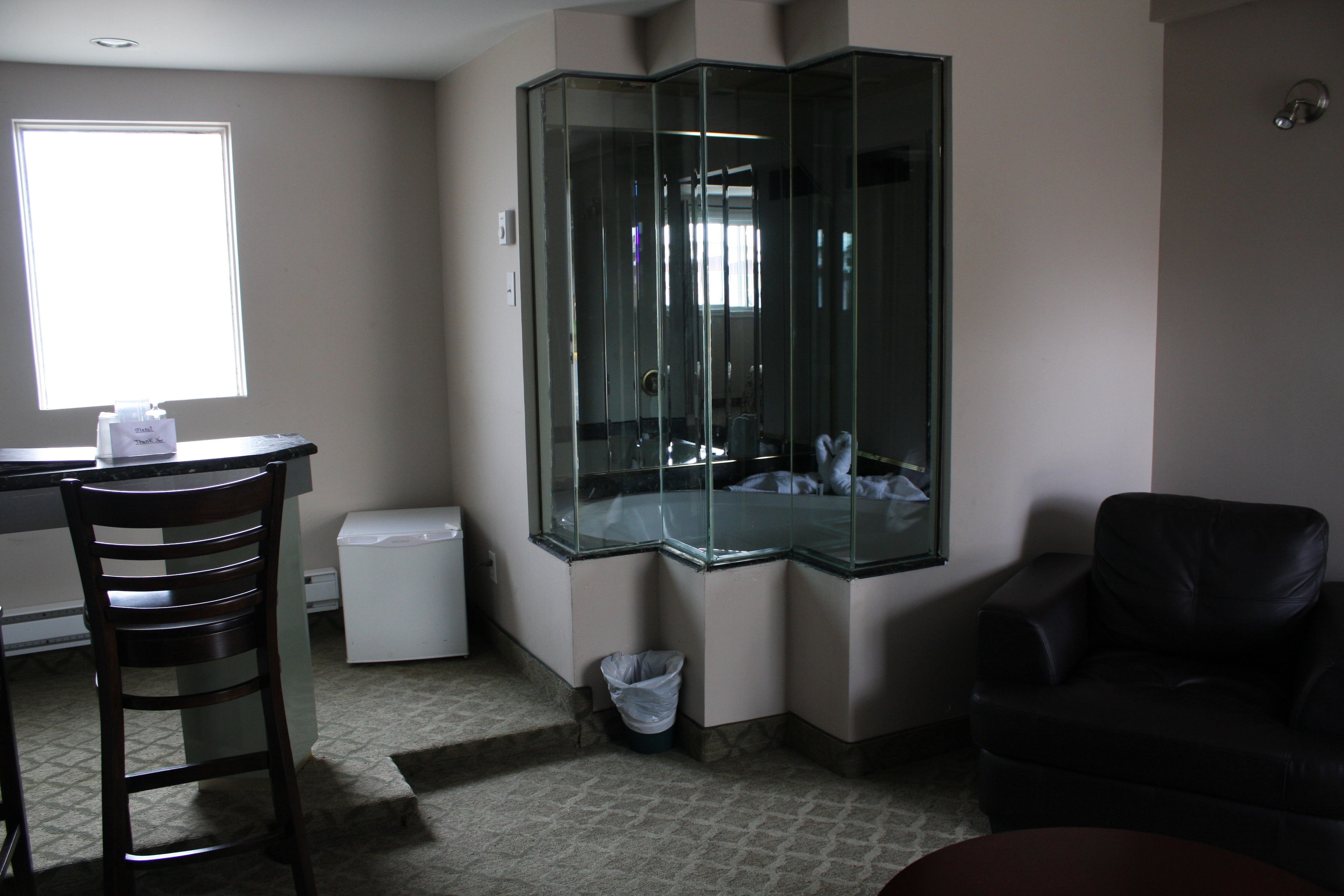 A room with a glass partition, a desk, a chair, a trash bin, and a couch.