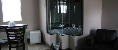 A room with a glass partition, a desk, a chair, a trash bin, and a couch.
