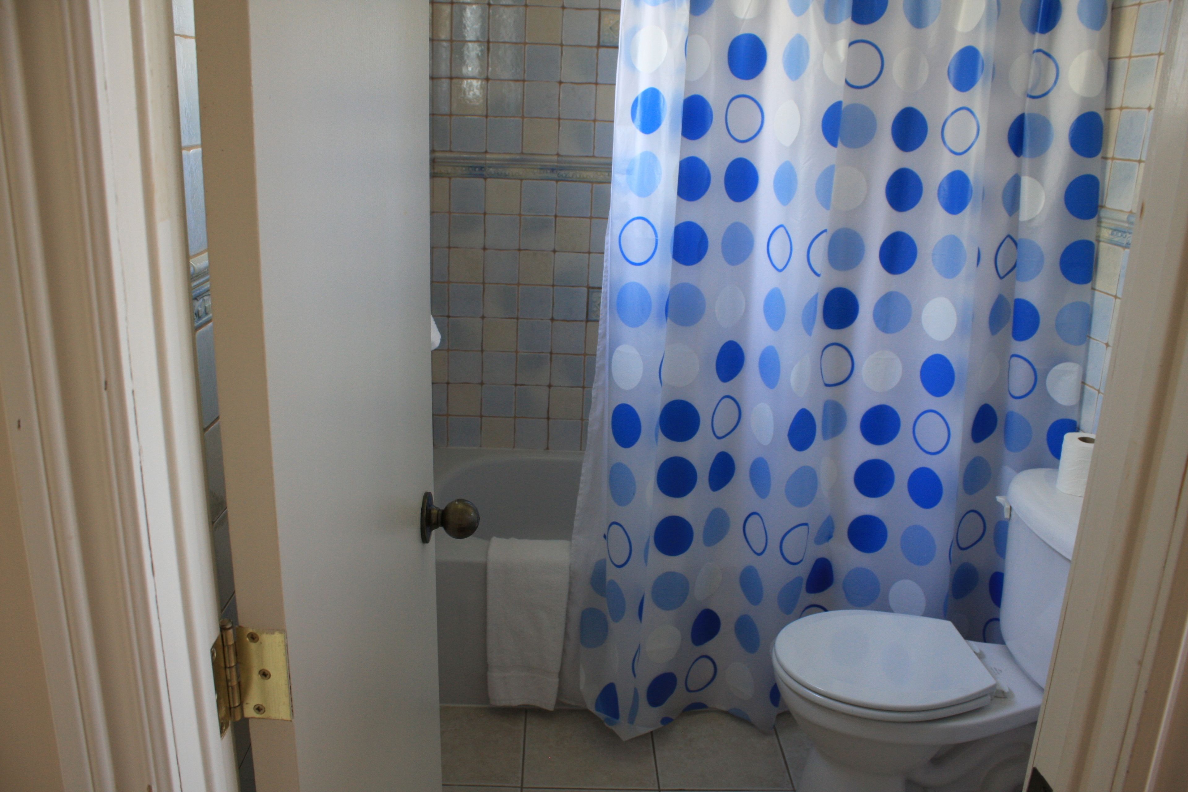 A bathroom with a toilet, a shower curtain with blue polka dots, and a tiled floor.