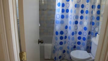 A bathroom with a toilet, a shower curtain with blue polka dots, and a tiled floor.