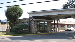 A gas station with a covered entrance, a large tree, and a building in the background. - Grand Motel Saint-Hubert (Longueuil)