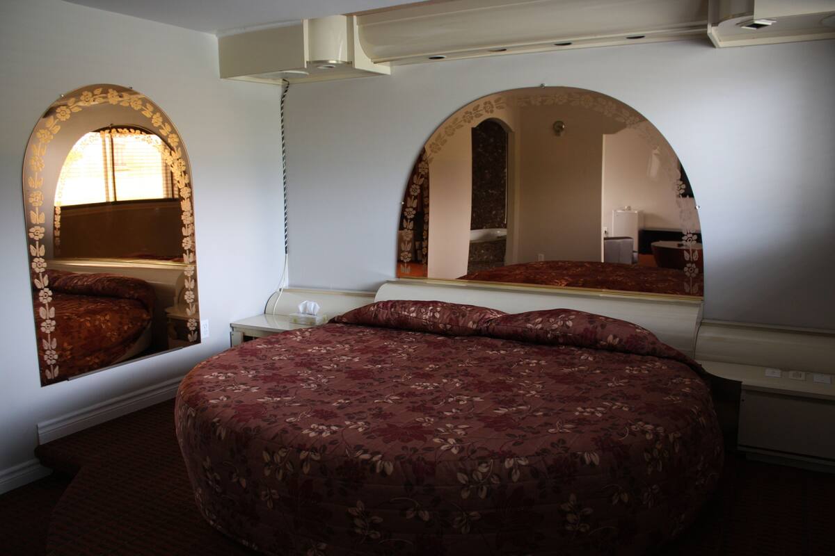 Un dormitorio con una cama grande, dos mesitas de noche, un espejo y una ventana con cortinas.