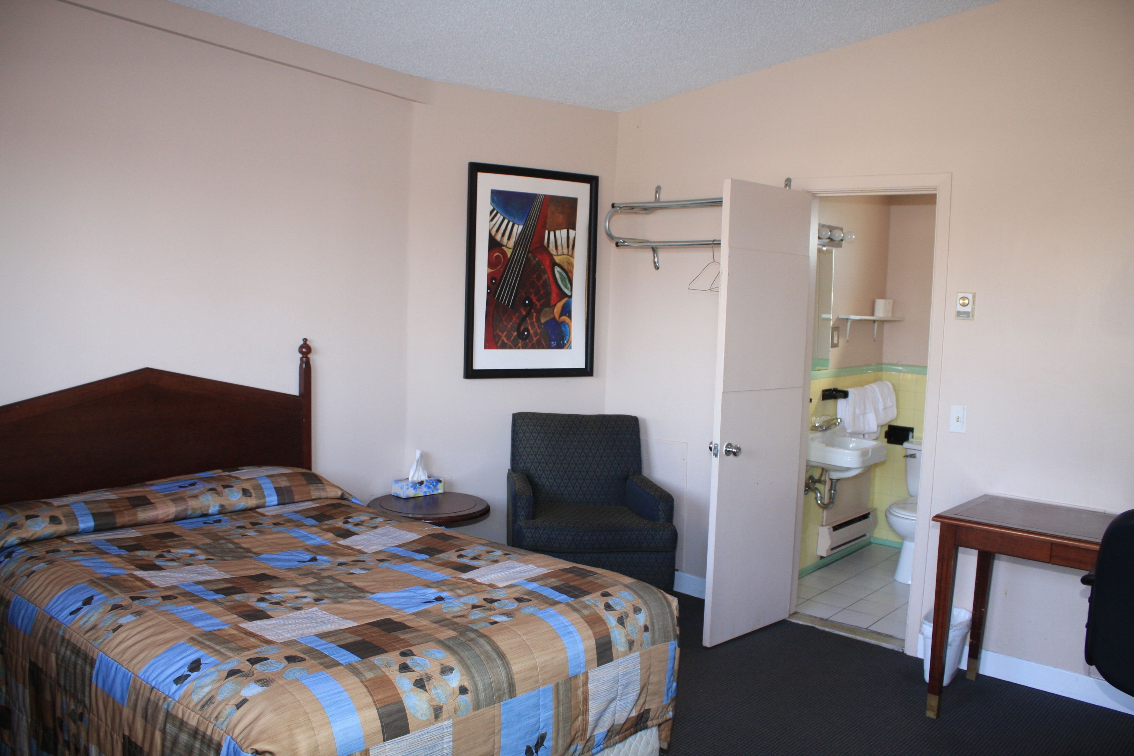 A hotel room with a bed, a chair, a desk, and a bathroom visible through an open door.