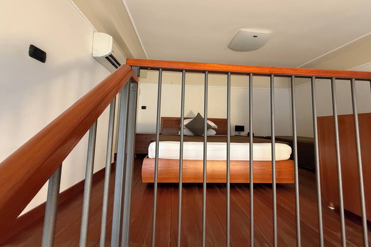 A bedroom with a wooden bed, a nightstand, and a wall-mounted light fixture.