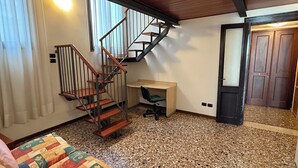 Una habitación con escalera de madera, un escritorio, una silla y un sofá colorido.