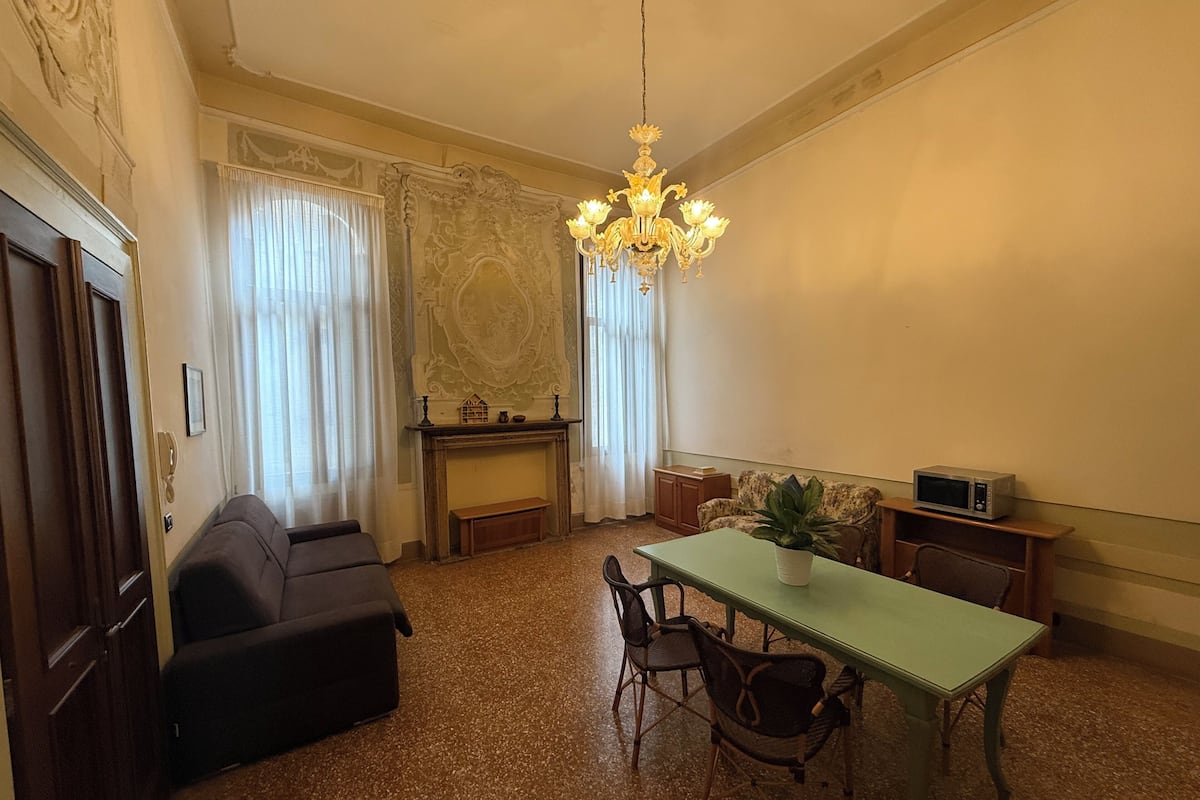 A room with a dining table, chairs, a sofa, a fireplace, and a chandelier.