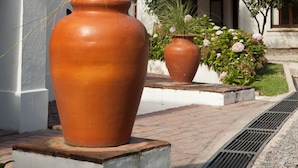 Un grand pot en terre cuite contenant des plantes, un lampadaire et un bâtiment à la façade blanche avec une fenêtre.