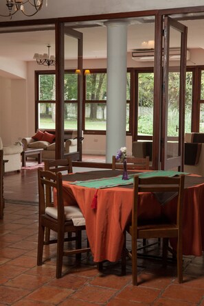 Un coin repas avec une table dressée pour quatre personnes, entouré de chaises en bois, d’un canapé et d’une fenêtre donnant sur un paysage verdoyant.
