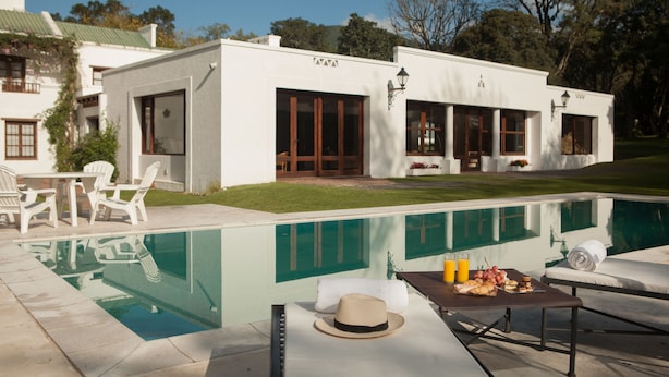 Une maison moderne dotée d’une piscine, de mobilier d’extérieur et d’une table à manger où sont disposés des plats et des boissons.