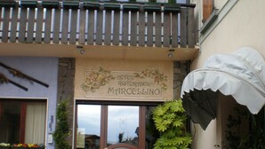 A hotel entrance with a wooden balcony, potted plants, and outdoor seating.