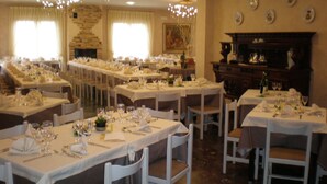 A formal dining room with multiple tables set for a meal, white chairs, and a fireplace in the background.