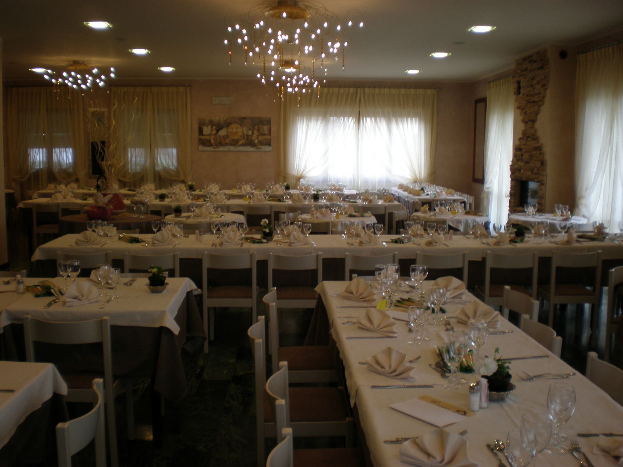 A banquet hall with multiple round tables set for dining, each with white tablecloths and neatly arranged place settings.