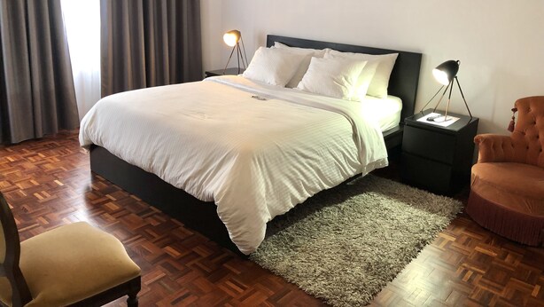 Une chambre à coucher bien rangée, avec un grand lit, une table de chevet avec une lampe, une chaise et un tableau accroché au mur.
