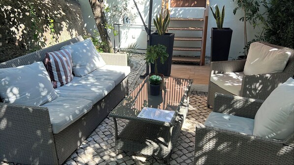 A sunlit outdoor seating area with wicker furniture, including a sofa and chairs, and a central table with a menu.