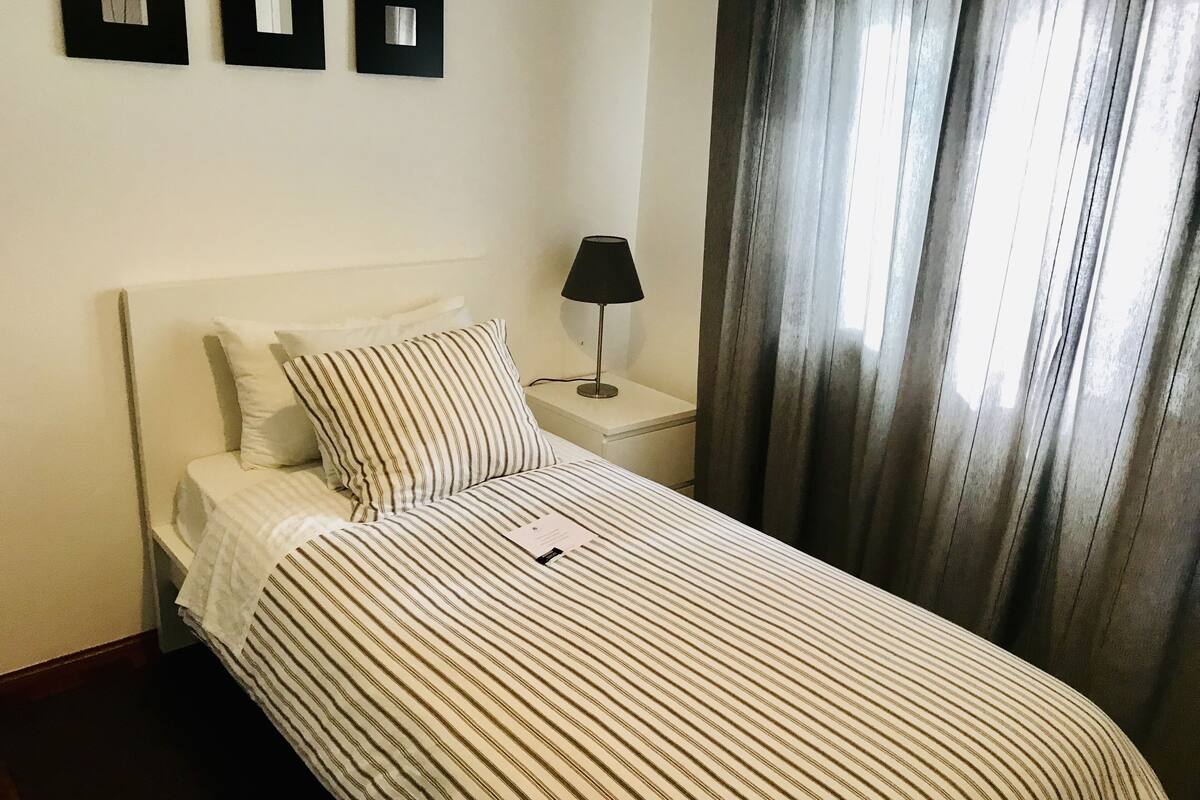 Un lit bien fait, avec une literie à rayures, une lampe de chevet et un tableau encadré au mur.