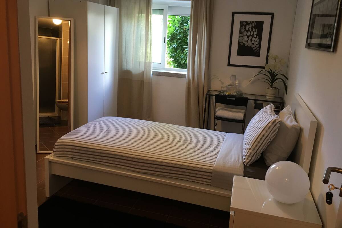 Une chambre d’hôtel avec un lit, une table de chevet, une lampe et une fenêtre avec des rideaux.