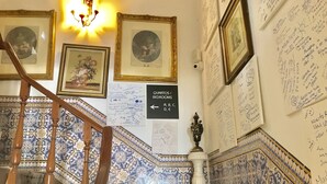 Un escalier recouvert de carreaux bleus et blancs formant un motif, une main courante en bois et un panneau indiquant l’emplacement des chambres d’hôtes.