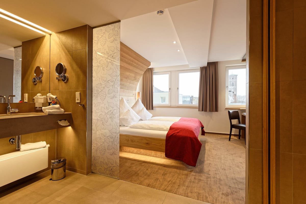 A hotel room with a bed, a bathroom with a mirror, a sink, and a chair.