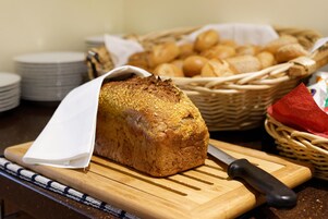 Una hogaza de pan sobre tabla de cortar con un cuchillo, rodeada de platos y cestas de pan.