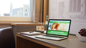 Ein Laptop auf einem Schreibtisch mit Blick aus dem Fenster, eine Flasche und eine Schüssel mit Trauben.