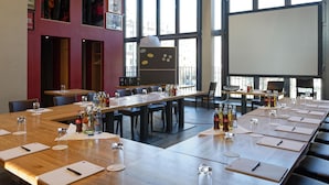 Ein Konferenzraum mit langen Tischen, Stühlen und einer Projektionsleinwand.