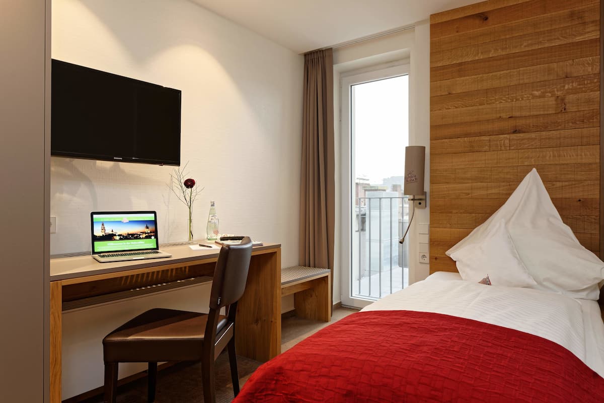 A hotel room with a bed, a desk with a laptop, a TV, and a window with curtains.