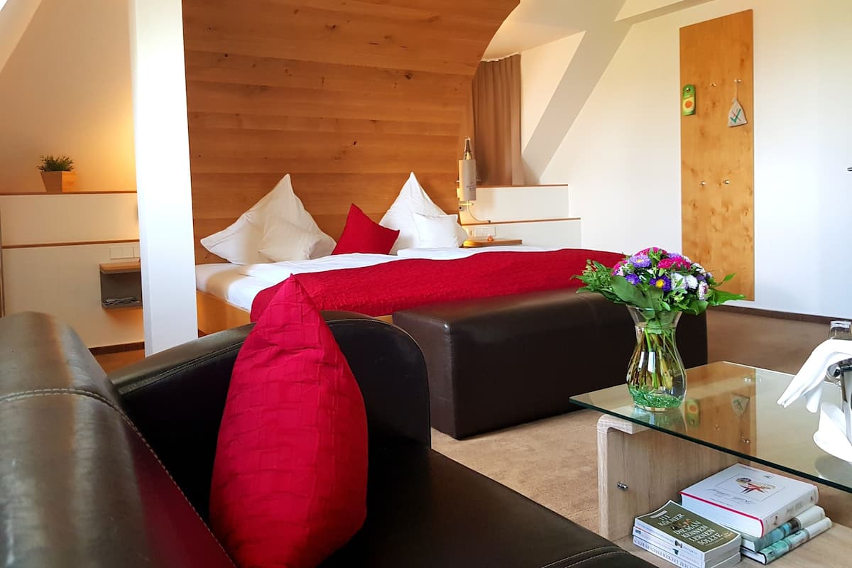 A modern hotel room with a wooden ceiling, a bed with red and white bedding, a glass coffee table with books, and a small plant on the nightstand.