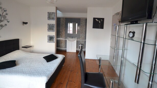A modern bedroom with a bed, a TV, a glass cabinet, and a bathroom visible in the background. - Hotel Le Palma (Angouleme)
