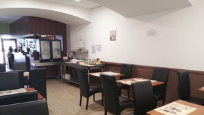 A restaurant with booths and tables, a kitchen area, and a counter. - Hotel Le Palma (Angouleme)