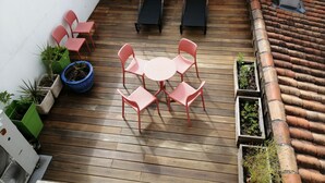 A wooden deck with a round table and six chairs, surrounded by potted plants and a blue pot. - Hotel Le Palma (Angouleme)
