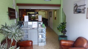 A reception area with a desk, chairs, potted plants, and a hallway leading to a room. - Hotel Le Palma (Angouleme)