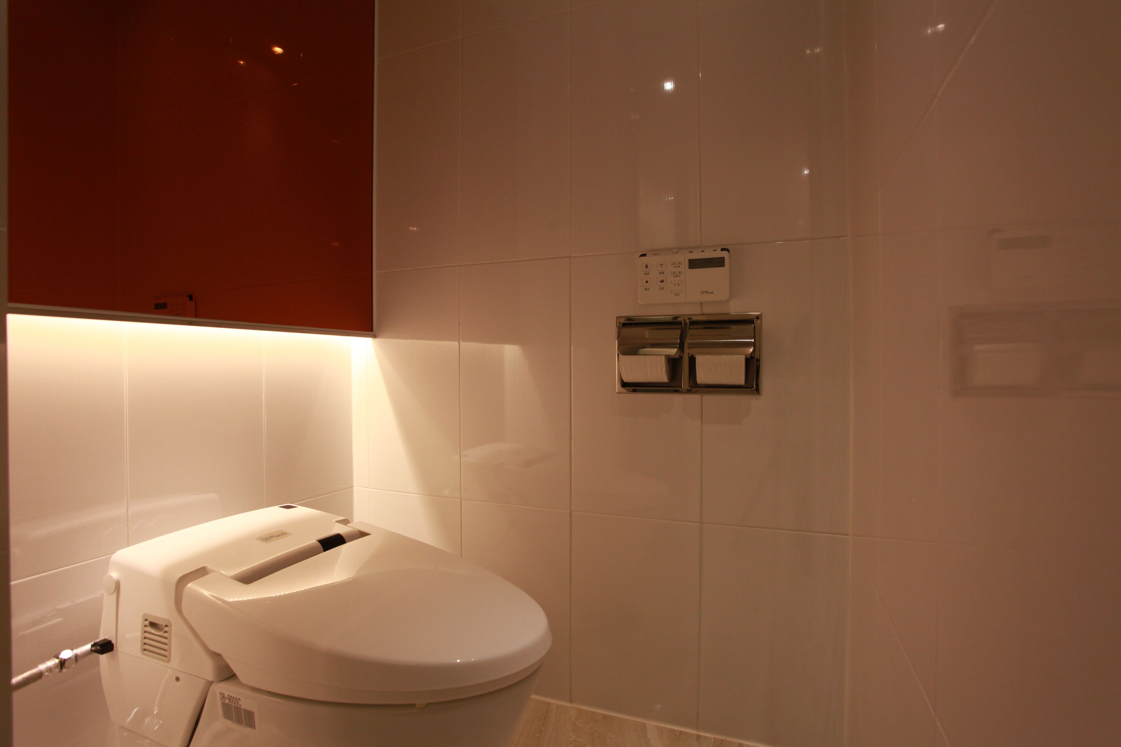 A modern bathroom with a white toilet, a wall-mounted bidet, and a control panel.