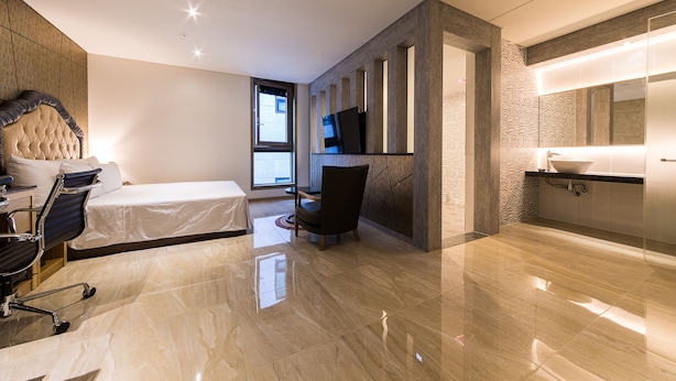 Een moderne hotelkamer met een bed, een bureau, een stoel, een televisie en een badkamer met een grote spiegel en wastafel.